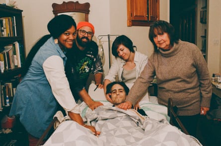 Friends and family pose with a man in a hospital bed at home