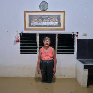 A woman stands shin deep in flood water inside a house next to a white wall