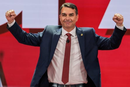 Flávio Bolsonaro on stage with arms outstretched and fists clenched