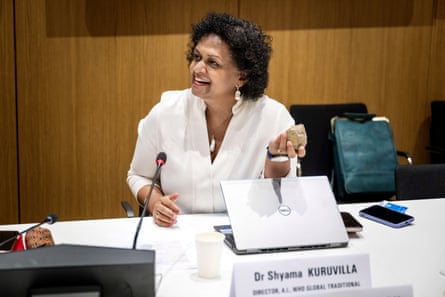 A woman in a white blouse speaks into a microphone.