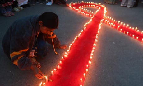 A person lights candles around a large red ribbon on the ground