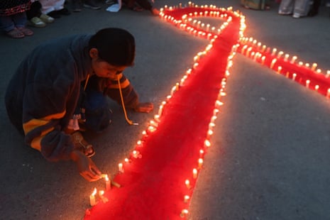 A person lights candles around a large red ribbon on the ground