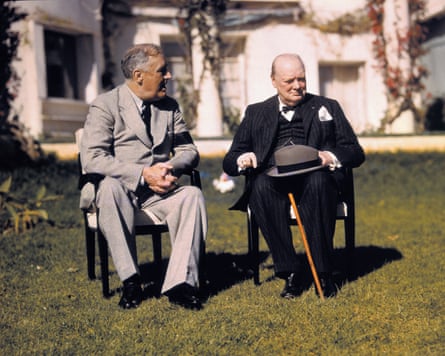 Franklin D Roosevelt in a grey suit and Winston Churchill in black, resting a bowler hat on his knees and a walking stick between them, side by side in chairs on a villa lawn