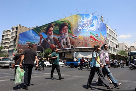 People in Tehran, Iran, walk past a large billboard featuring the late Iranian supreme leaders Ruhollah Khomeini and Ali Khamenei.
