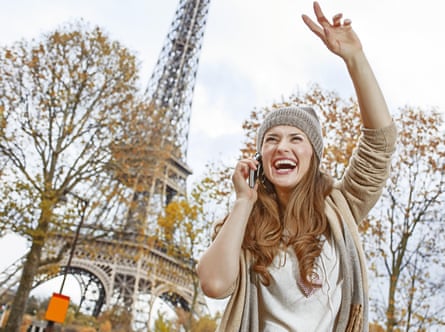 A happy young woman in Paris, France, using a mobile phone and waving