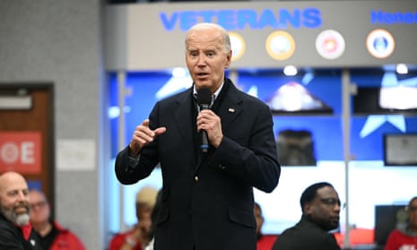 White man wearing suit holds a microphone and gestures.