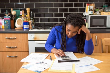 Person sits at the kitchen table, looking at bills and using a calculator
