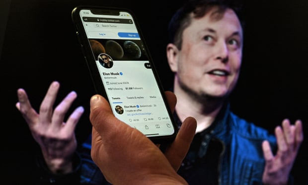 A phone screen displays the Twitter account of Elon Musk with a photo of him shown in the background