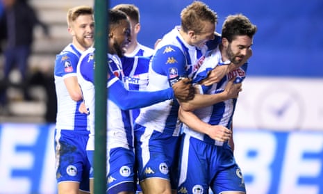 Will Grigg is mobbed by his team-mates after scoring Wigan’s winner against Manchester City to reach the quarter-finals.