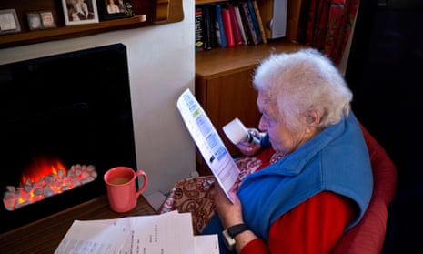 Older women at home in front of fire using a magnifier to read her latest household energy bills