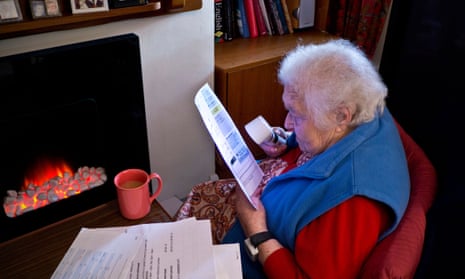 Elderly person looking at bill by electric fire place.