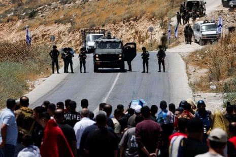 A crowd of Palestinians stand on a road in a face-off with Israeli soldiers.