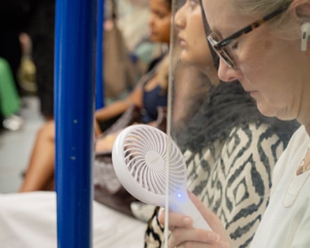 A traveller who has her eyes closed tries to keep cool with a handheld fan.