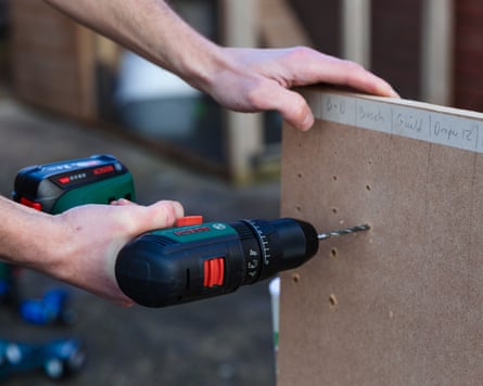 A man drills a hole into a wooden plank with a Bosch drill
