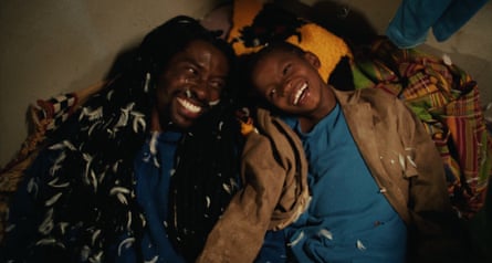 A man and a boy lie on their backs, covered in feathers, laughing.