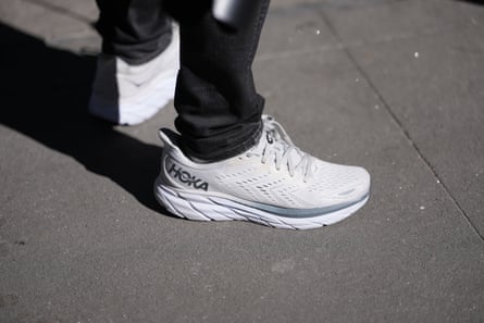 A guest at New York fashion week wears black denim straight-leg jeans with white mesh Hoka Clifton 8 sneakers in February 2026.