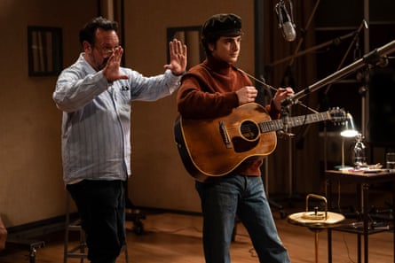 man plays guitar while another man stands behind him holding up his hands