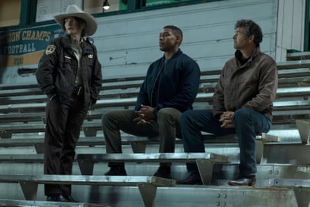 Kelly Macdonald in a sheriff’s hat stands on the bleachers while Aaron Pierre and Kyle Chandler sit in Lanterns.