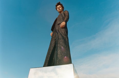 Harry Styles standing on white box, shot against blue sky background