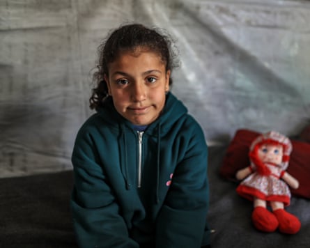 A 12-year-old girl in a green hoodie with a red doll by her side