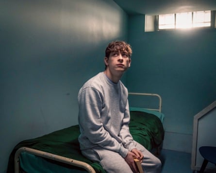 James sits on a bed in a prison cell, looking up into a corner of the room