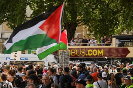 A rally in London with lots of people and a tourist bus and flags