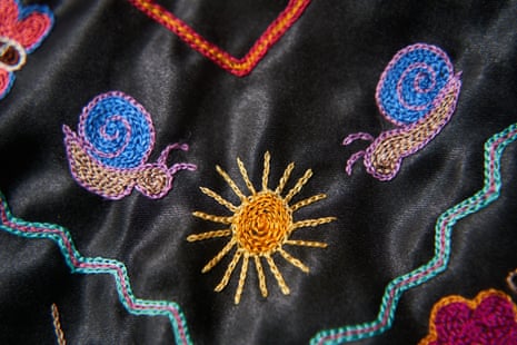 A black cloth with colourful embroidery of snails and a sun on it