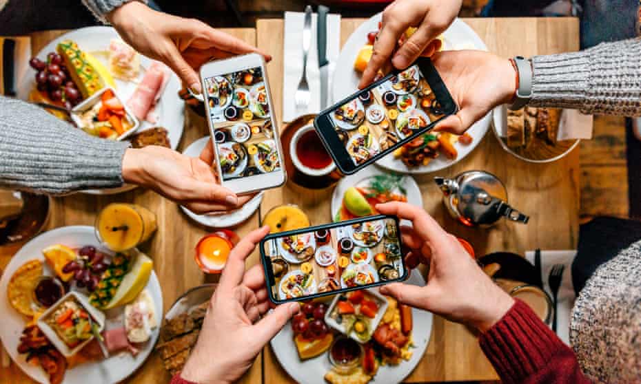 Friends taking pictures of food on the table with smartphones in a restaurant.
