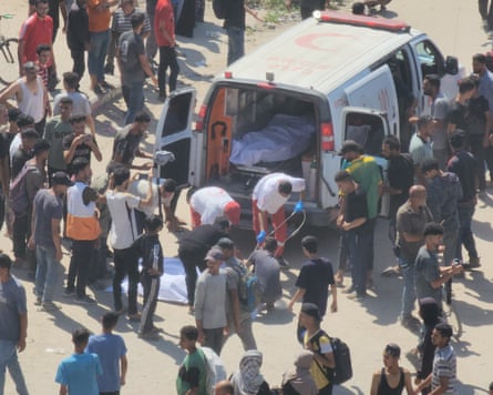 Dead bodies shrouded in white sheets are placed into an ambulance