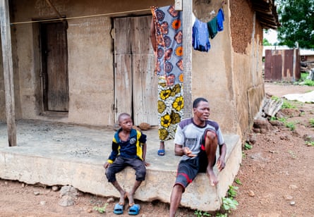 A man and boy sit on the porch of a simple concrete house in Nigeria.
