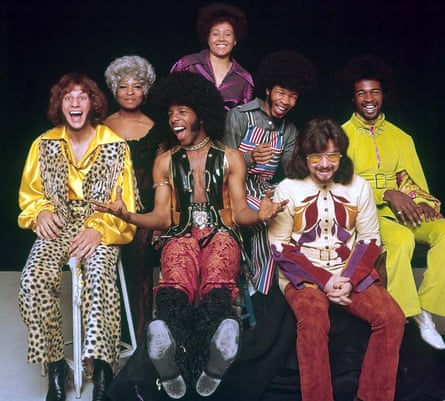 They pose for a photo, most of the group smiling, Sly Stone gesticulating with his hands