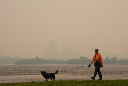 A woman walks her dog along the Ottawa River in Ottawa on June 6 as wildfire obscures distant Gatineau, Quebec.