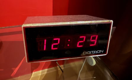 A clock with what looks like a wooden surround with a black face and lit-up red digital display
