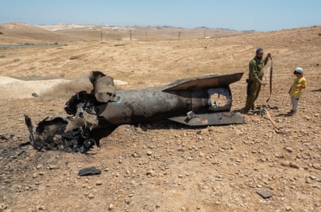 Um soldado israelense e seu filho estão ao lado dos restos de uma balística iraniana contra uma paisagem desértica.