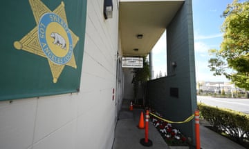 Orange plastic poles strung with yellow police tape along the cement entrance to a building, with a gold police star painted on a green background.