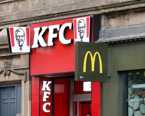 KFC and McDonald's storefronts side by side beneath a weathered stone building facade