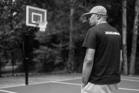 A man wearing a T-shirt and a cap stands on a basketball court