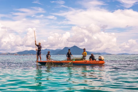 A group of Bajau men fishing with a net in a dugout boat.