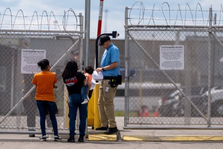 two women holding young children stand outside a metal fence