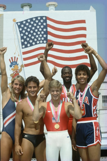 American gold medallists at the 1984 Games stand together arms aloft in front of a poster with a picture of an American flag flying.