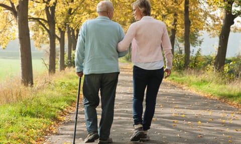 Older couple walk arm in arm along a path lined with trees