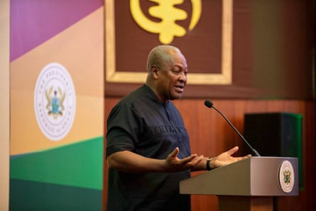 he is making a speech in a formal conference room with wooden panelling and the presidential crest; he wears a short-sleeved black shirt.