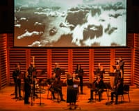 Phaedra Ensemble musicians perform with instruments below a screen showing clouds