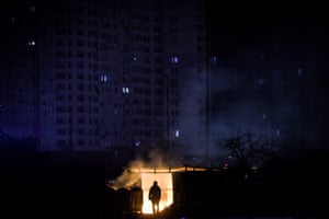 A man stands near burning garbage in front of an apartment building during a scheduled power cut in Kyiv, Ukraine