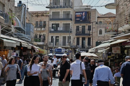 A crowded street with an advert showing Itamar Ben-Gvir on a building.