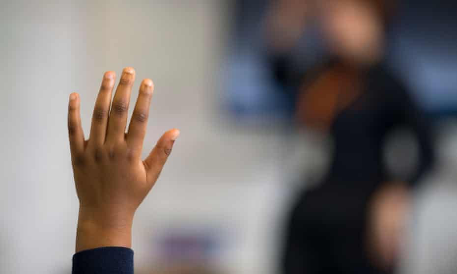 A black child's hand held up in a school class