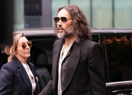 Russell Brand walking to court holding hands with his wife.