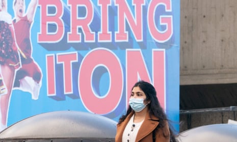 A woman wearing a face mask in central London stands under a poster that reads ‘Bring it on’