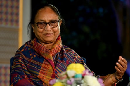 A woman wearing glasses and a bright woven shawl gestures during a conversation.