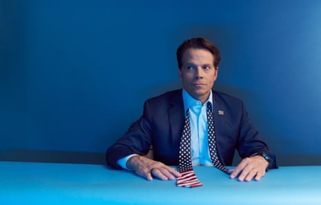Anthony Scaramucci sitting at a bright-blue desk with his hands on the table, wearing a light-blue open-necked shirt, a dark-blue blazer and an untied stars and stripes tie, facing the camera with his eyes looking to his right
